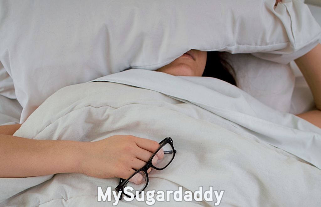 woman oversleeping with a pillow on her head and holding her glasses